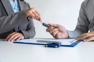 Photo of two people finalizing a contract and exchanging keys depicting the Nissan lease payment case recently settled by Schlanger Law Group